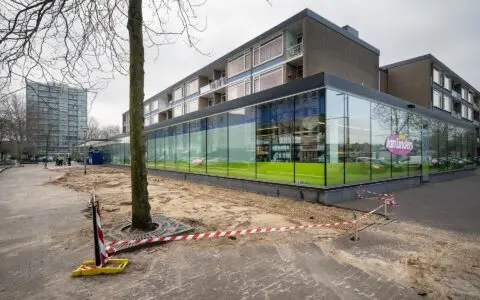 Een foto van de situatie voor de werkzaamheden. We zien een gebouw, een boom en een stuk bestrating.