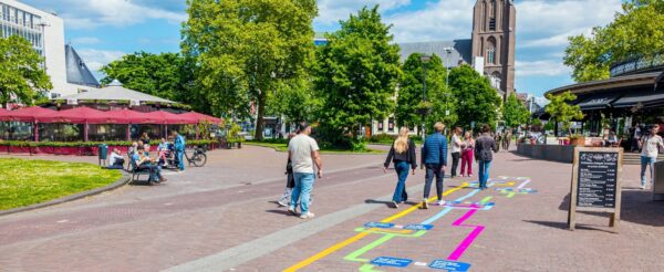 Inwoners lopen op het Velperplein over een hinkelpad met duurzame keuzes.
