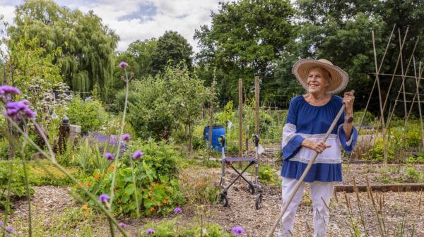 Mevrouw staat in haar moestuin met een hark in de hand.