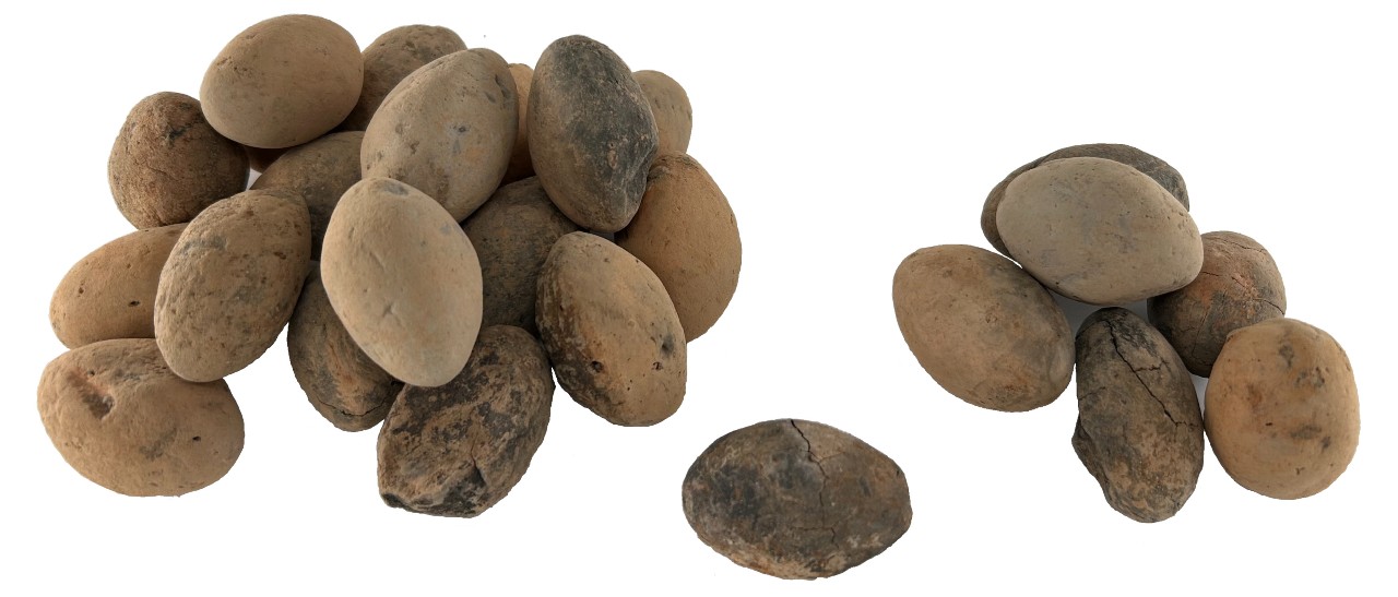 25 slingerkogels van klei. De vorm van deze kogels is rond in het midden en loopt aan beide kanten uit in een punt (eivormig). De kleur van de kogels is beige, lichtbruin met donkere vlekken.